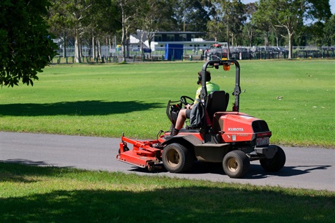 commercial front-mounted mower, as it travels along a paved path in the park, during a sunny day